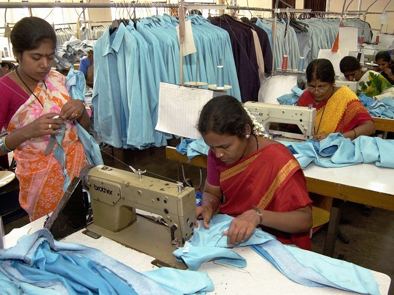 Women wearing red outfits sewing a blue garment on a white table